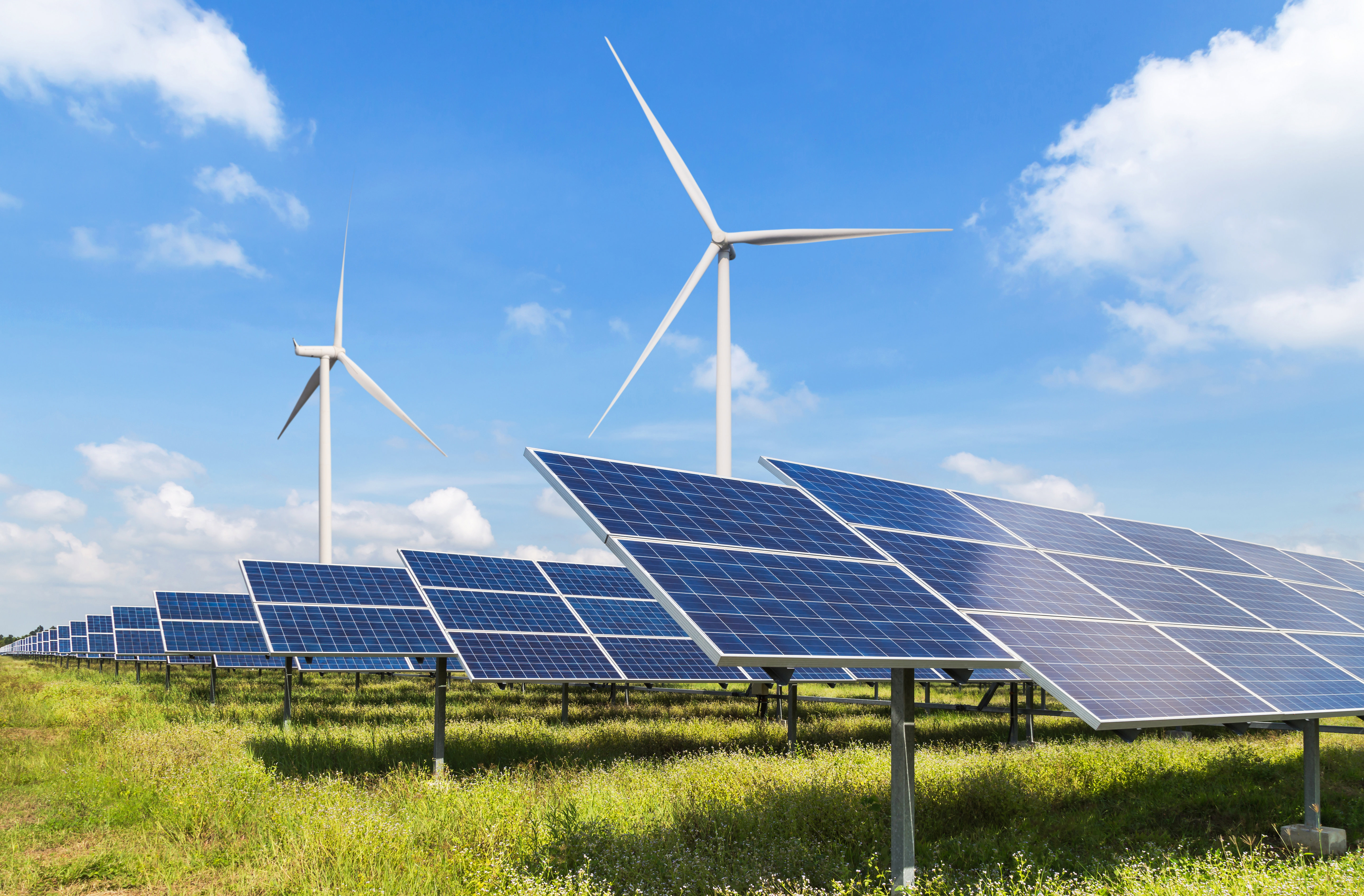 Wind turbines in a field with solar panels while the sun shines